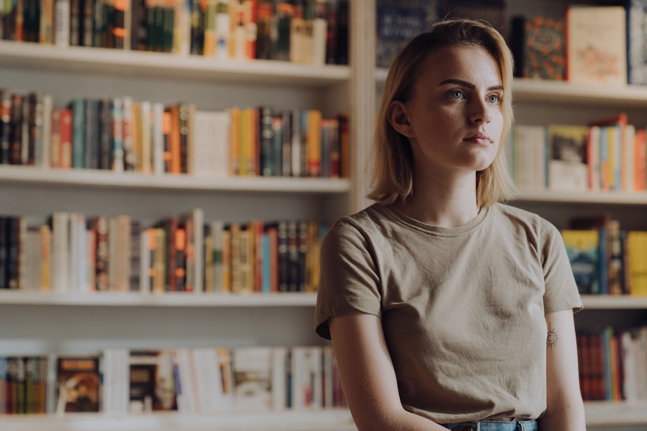 Woman in Gray Crew Neck T-shirt Standing Near Books